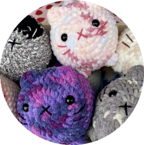 Pile of crochet cats that are pink, purple, gray, and white