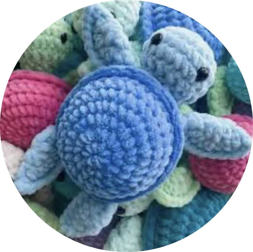 Many crochet turtles in a pile with a blue crochet turtle on top