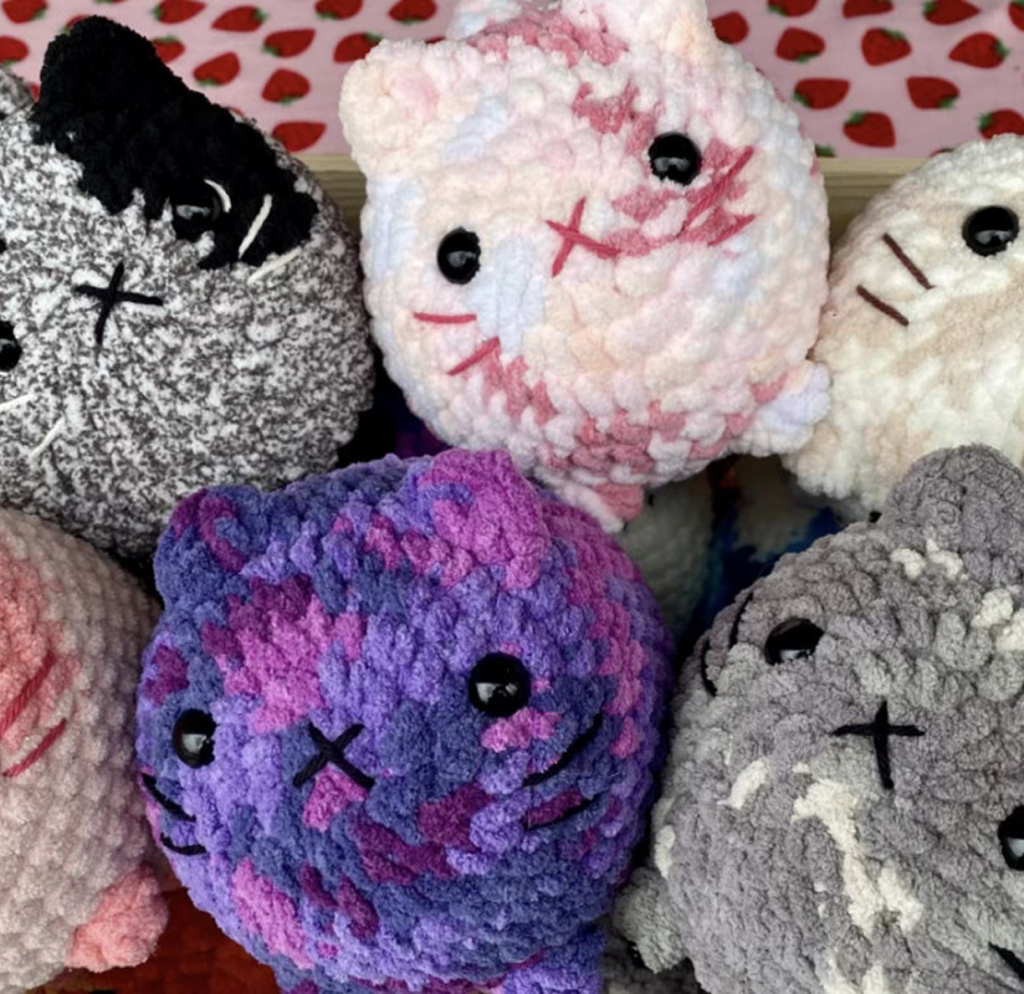 Pile of crochet cats that are pink, purple, gray, and white